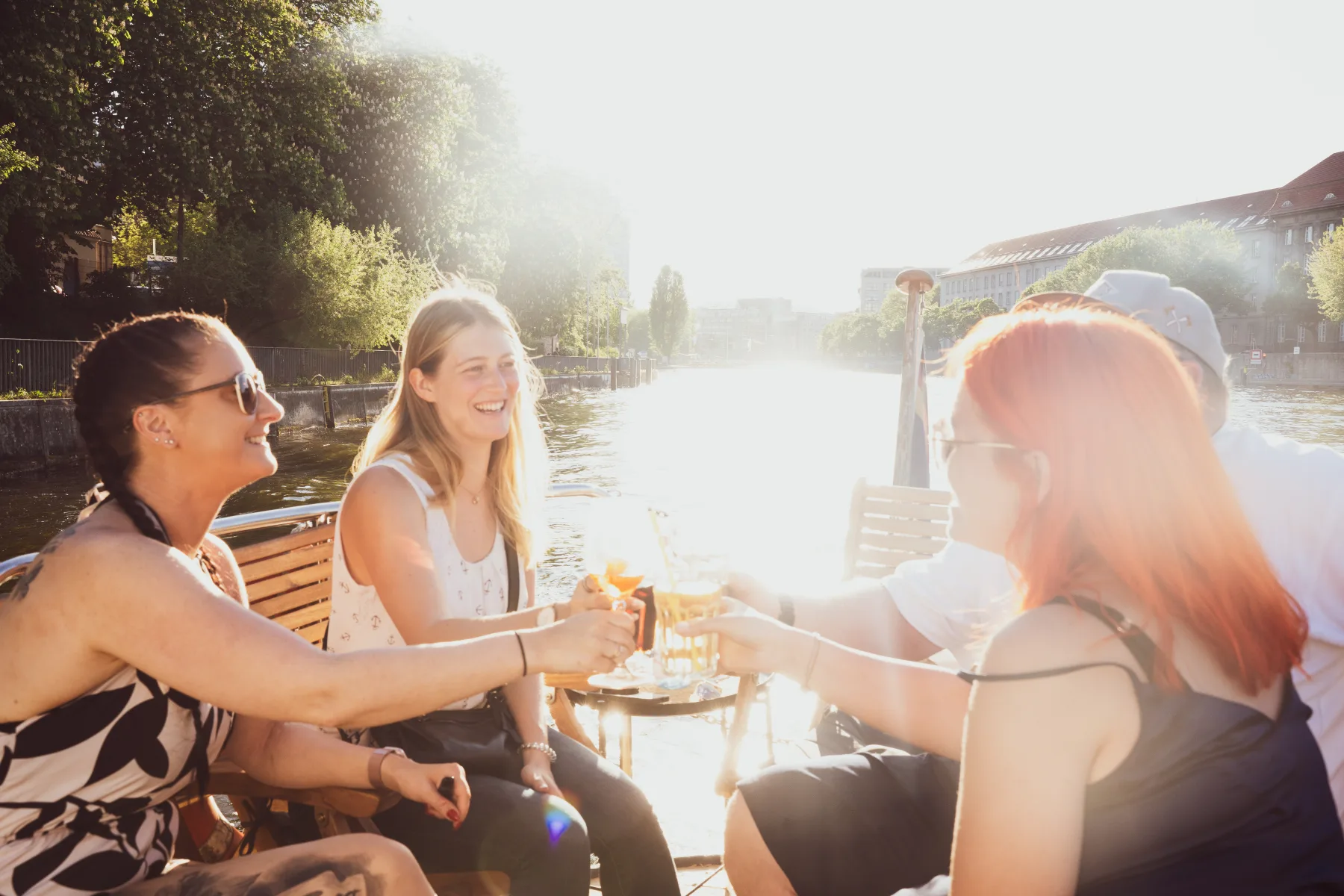 Freunde stoßen gemeinsam an Bord an, im Hintergrund die Spree in Berlin